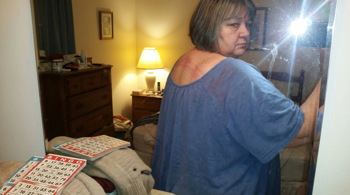 A woman turning in front of a bedroom mirror to look at her shoulder