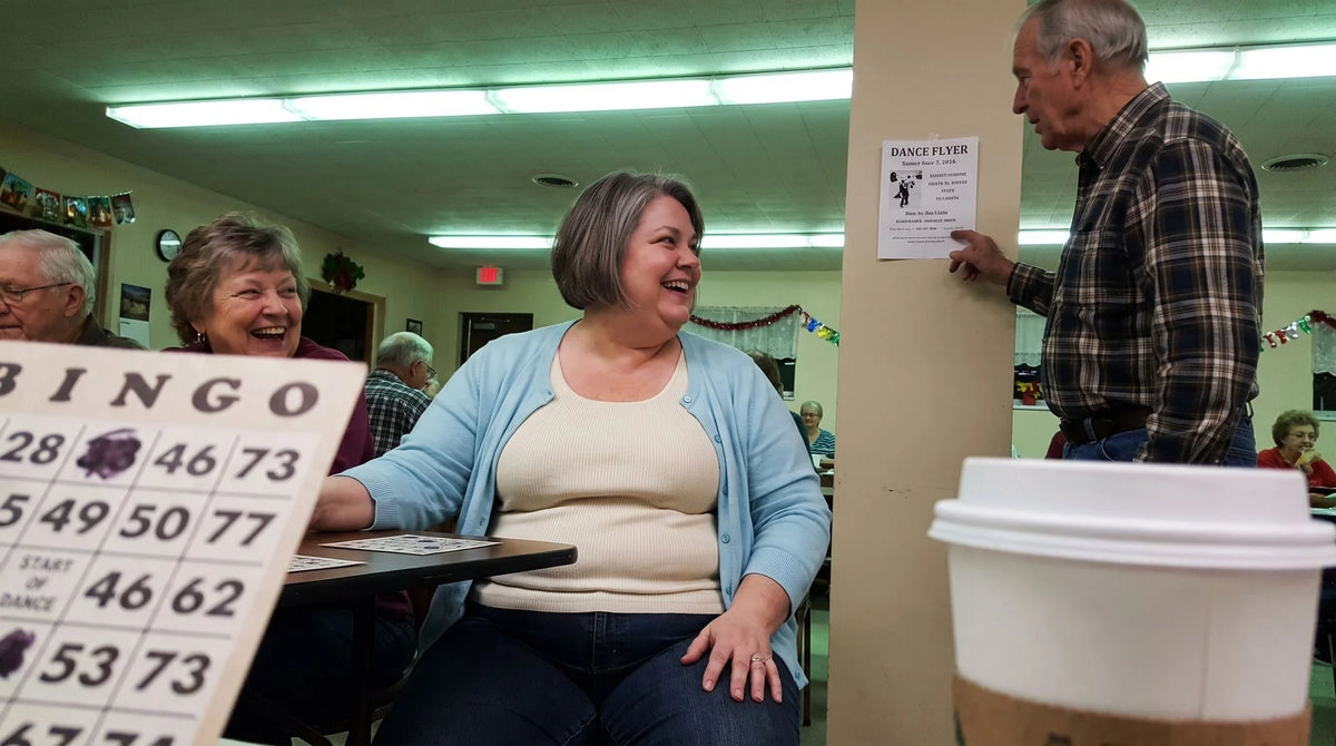 Two friends laughing at the bingo table as a man stops by to talk
